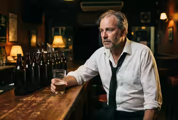Simpatia para parar de beber, homem cabisbaixo diante de várias garrafas num bar